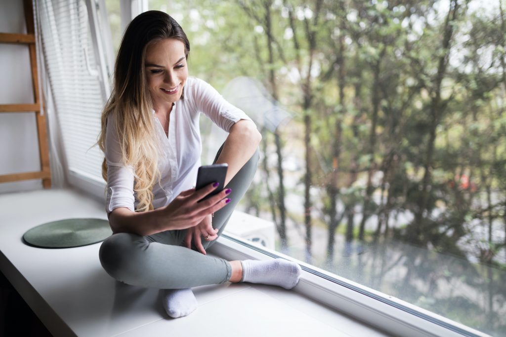 Beautiful woman using cell phone at home to connect to social media networks